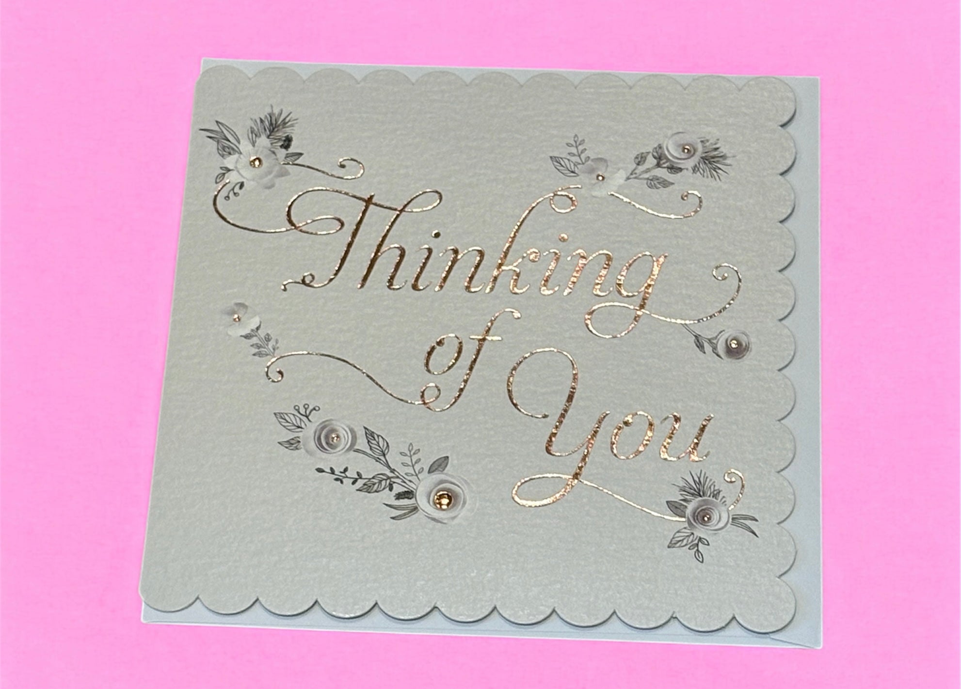 A braille greeting card with the text 'Thinking of You' on the front, decorated with silver floral designs against a beige background.