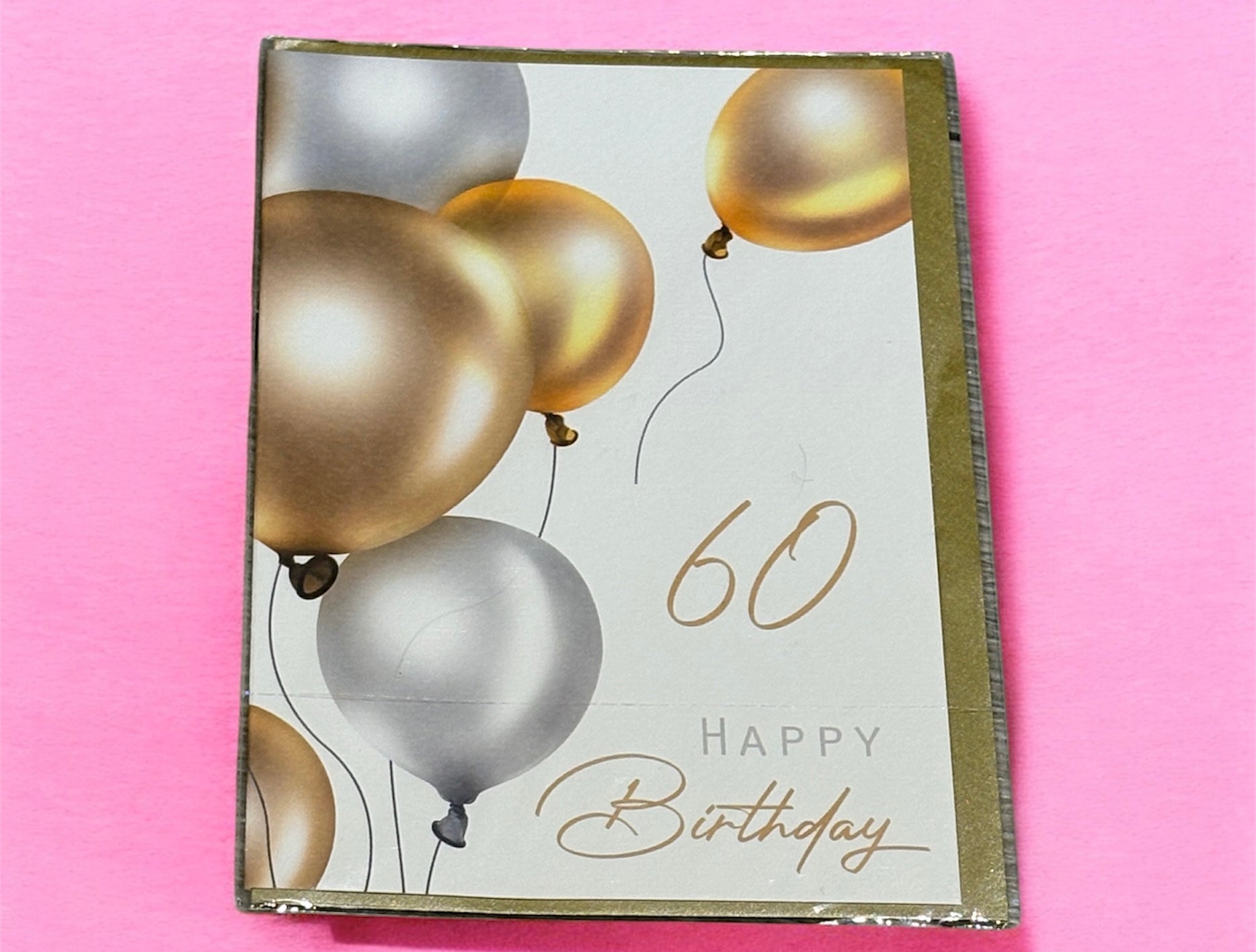 A Braille birthday card with a white background, featuring metallic gold and silver balloons and the text '60 Happy Birthday'.